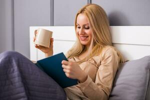 Beautiful woman enjoys reading a book at her bedroom and drinking tea or coffee. photo