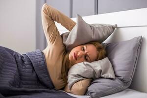 Angry woman disturbed with a noise trying to sleep and covering her ears with a pillow. photo