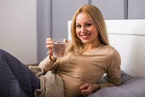 Beautiful woman drinking water and sitting on bed. photo