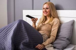 Beautiful woman enjoys watching tv at her bedroom. photo