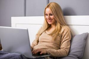 Beautiful woman enjoys using laptop at her bedroom . photo