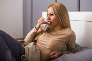 Beautiful woman drinking water and sitting on bed. photo