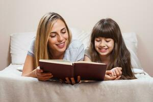 Mother and daughter reading together book in bed photo