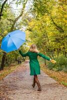 mujer participación paraguas y otoño hojas mientras saltando y caminando en el parque. foto