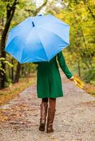 Woman holding umbrella and fall leaves while walking in the park. photo