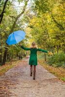 mujer participación paraguas y otoño hojas mientras saltando y caminando en el parque. foto