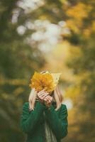 Woman covering her face with fall leaves while enjoys in autumn and spending time in the park. photo