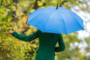 mujer participación azul paraguas y comprobación para lluvia mientras en pie en el parque. foto