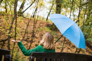 Woman holding blue umbrella and checking for rain while sitting in the park. photo