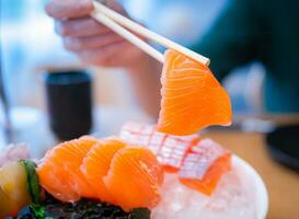 utilizando palillos, salmón sashimi. sashimi es un popular plato de japonés restaurantes foto