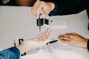 A car rental company employee is handing out the car keys to the renter after discussing the rental details and conditions together with the renter signing a car rental agreement. Concept car rental. photo