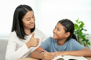 Mother teaching lesson for daughter. Asian young little girl learn at home. Do homework with kind mother help, encourage for exam.. Girl happy Homeschool. Mom advice education together. photo