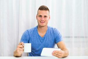 Young man enjoys drinking coffee and using digital tablet at home. photo