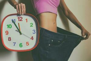 Woman in large jeans holding clock.Weight loss concept.Toned photo