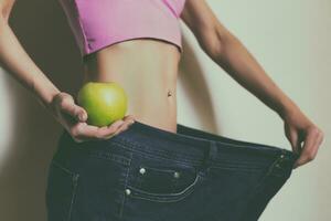 Woman in large jeans holding apple.Weight loss concept.Toned photo. photo