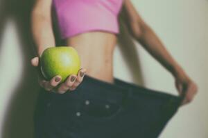 Woman in large jeans holding apple.Focus on apple.Weight loss concept.Toned photo. photo