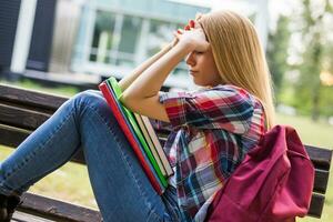 Exhausted and worried female student studying outdoor. photo