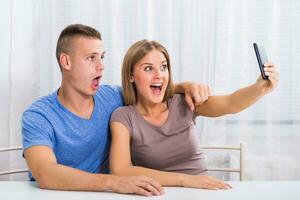 Young happy couple sitting at the table and taking selfie. photo