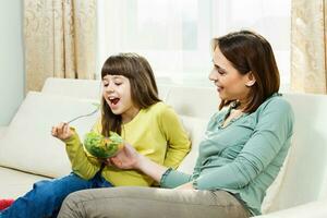 hija comiendo vegetales y su madre es contento acerca de eso foto