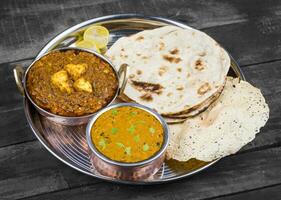 Indian Traditional Thali Food Dal Makhani Served with Chapati, Papad, Kadai Paneer or Lemon on Vintage Wooden Background photo