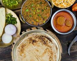 indio cocina chapati con sev tamatar, gatta curry, raita, papad o cebolla en de madera antecedentes foto