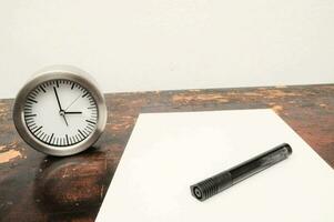 a clock and pen on a table next to a notepad photo