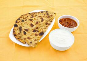 indio tradicional desayuno plato aloo paratha servido con Fresco Cuajada y pepinillo foto