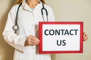 Image of female doctor holding a paper with a text  contact us. photo