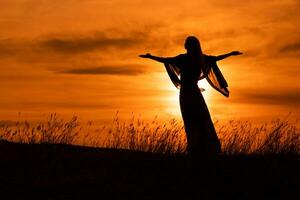 silueta de un mujer con brazos extendido mirando a hermosa puesta de sol. foto