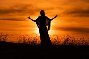silueta de un mujer disfruta meditar a hermosa puesta de sol. foto