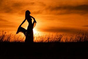 contento mujer bailando y participación bufanda mientras disfruta gasto hora a puesta de sol. foto