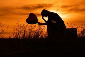 silueta de un triste mujer sentado en maleta con corazón conformado globo a el puesta de sol. foto