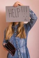 Woman holding empty wallet and paper with word help while standing in front of wall photo