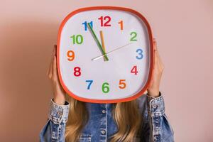 Woman holding clock while standing in front of wall. photo