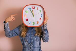 Woman holding clock while standing in front of wall. photo