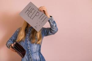 Woman holding empty wallet and paper with word help while standing in front of wall photo