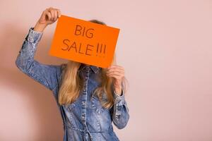 Woman holding paper with text big sale while standing in front of the wall. photo