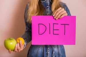 Woman holding paper with word diet and fruit while standing in front of wall. photo