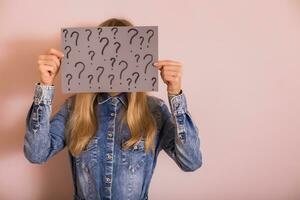 Woman holding paper with question marks while standing in front of the wall. photo