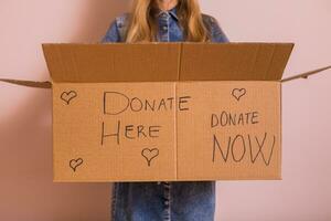 mujer participación donación caja mientras en pie en frente de muro.. foto