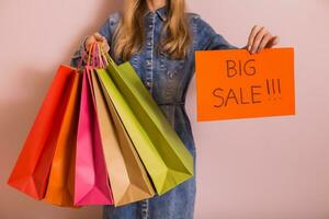 Woman holding shopping bags with paper with text big sale while standing in front of the wall. photo