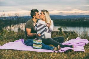 Happy couple enjoy kissing and  looking at their  baby clothing and relaxing outdoor. photo