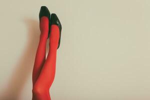 Beautiful legs  of a woman in red tights and high heels up in front of wall.Toned photo