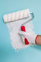 Image of man holding paint roller and painting blue wall. photo