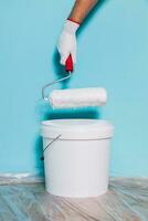 Image of paint can and man holding paint roller in front of blue wall. photo