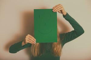 Woman with happy face on paper standing  in front of wall.Toned image. photo