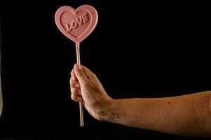 a person holding a pink heart shaped lollipop photo