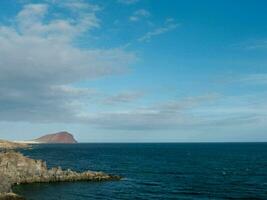 a rocky coastline with a blue sky and a small island photo