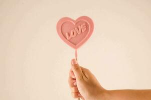 a pink heart shaped lollipop is held in a hand photo