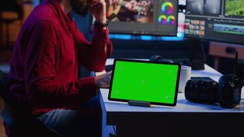 Green screen tablet on desk in multimedia agency next to video editor working for independent production company inputting music, dialogues, graphics and effects over raw footage